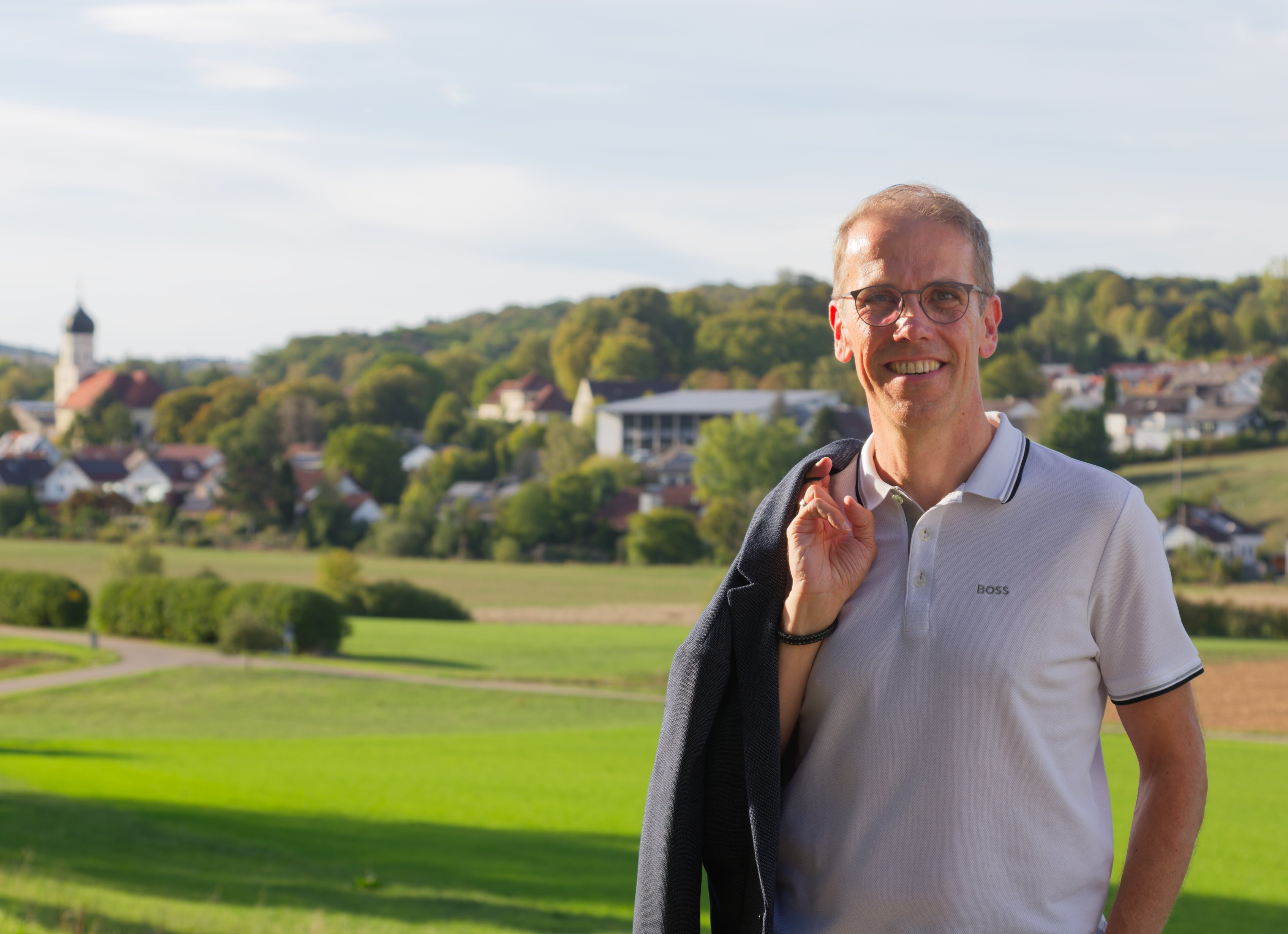 Michael Tropp lächelt in die Kamera, das Sakko über der Schulter, hinter ihm Westerstetten mit dem Kirchturm.